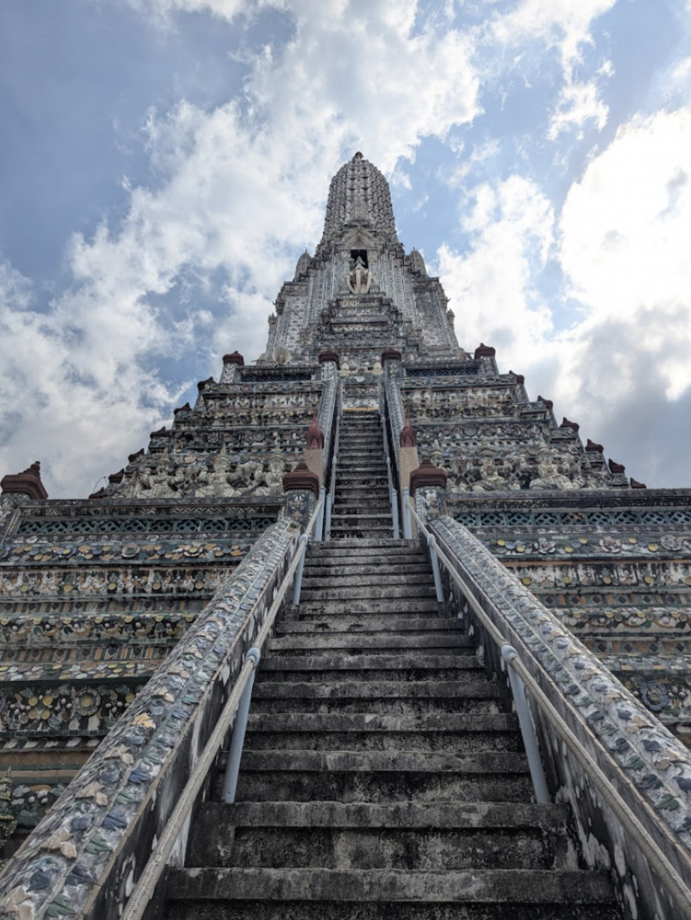 Tall stone temple with steep stairs under a partly cloudy sky.
